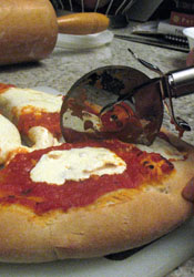 A pizza wheel cuts through toppings and crust